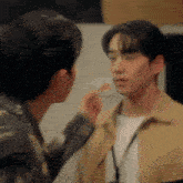two men are standing next to each other and one is touching the face of the other .