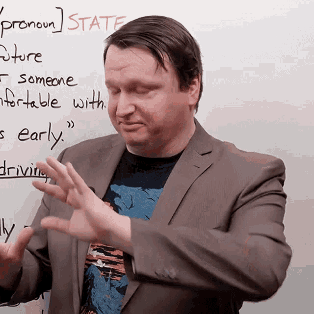 a man in a suit stands in front of a white board that says 