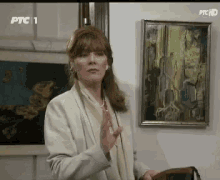 a woman is standing in front of a painting on a wall with ptc 1 on the screen