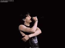 a man is singing into a microphone while standing on a stage with his arms crossed .