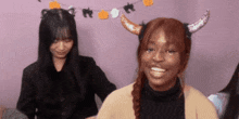a woman with horns on her head is smiling while another woman stands behind her