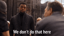 a man in a black suit is standing in front of a group of men and saying we don 't do that here .