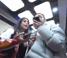 a man and a woman are in an elevator looking at their cellphones
