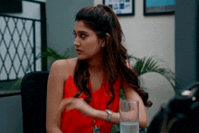 a woman in a red tank top is sitting at a desk with a glass of water