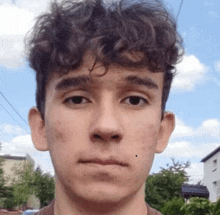 a young man with curly hair is standing in front of a blue sky .