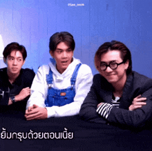 three men are sitting at a table and one of them is wearing overalls and a white hoodie