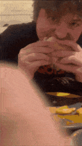 a man in a black shirt is eating a hamburger and french fries at a table .