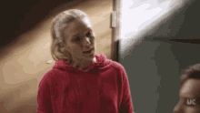 a woman in a red hoodie stands next to a man with the letters uc on his face