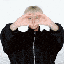 a man in a black jacket is making a heart with his hands