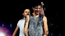 two men are standing on a stage and one is drinking water from a bottle