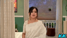 a woman in a white saree is standing in front of a window with the letters kk on the bottom