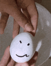 a person is holding a white egg with a face drawn on it .