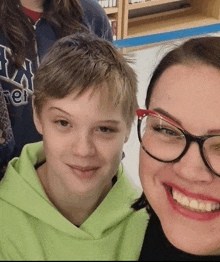 a woman wearing glasses and a boy wearing a green hoodie are smiling for a picture .
