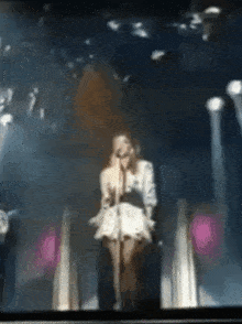 a woman in a white dress singing into a microphone on a stage