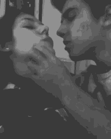 a black and white photo of a man and a woman kissing .