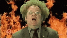 a man with green hair and glasses is standing in front of a fire