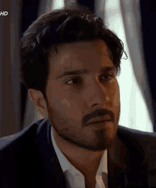 a man with a beard wearing a suit and white shirt is looking at the camera .