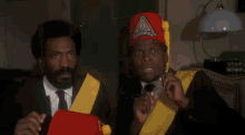 a man in a suit and tie wearing a red hat and a yellow sash .