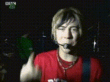 a man in a red shirt is wearing a microphone and giving the middle finger .