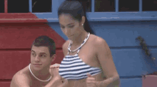 a man and a woman are standing next to each other in a pool . the woman is wearing a striped bikini top .