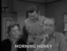 a black and white photo of a group of people sitting in a room with the words morning honey on the bottom .