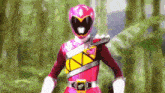 a pink power ranger is standing in the woods .