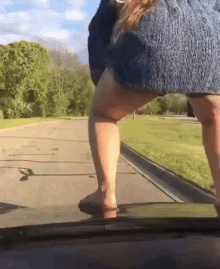 a woman is standing on the hood of a car on the side of the road