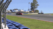 a red car is driving on a race track with a row of blue tires in the foreground