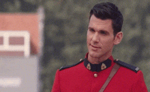 a man in a red uniform is standing in front of a building and looking at the camera .