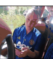 a woman wearing a blue manchester united jersey is looking at her phone