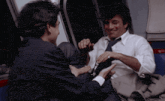 a man in a suit and tie is sitting next to another man in a white shirt