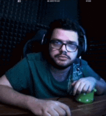 a man wearing glasses and headphones is sitting at a desk using a green mouse .