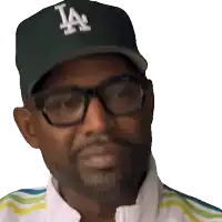 a man wearing glasses and a la hat looks at the camera