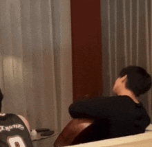 a man in a black jersey with the number 9 on it is sitting on a couch holding a guitar .