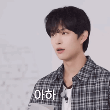 a young man wearing a plaid shirt is holding a notebook and says " 아하 " in korean