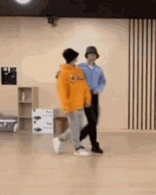 two men are dancing together in a room . one of the men is wearing an orange hoodie .