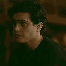 a young man with curly hair is wearing a black shirt and looking at something .