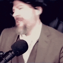 a man in a suit is talking into a microphone while wearing a hat .