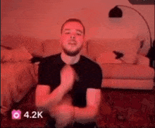 a man with a beard is sitting in a living room with a red light behind him .