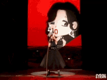a woman in a black dress singing into a microphone in front of a screen with the word syron on it
