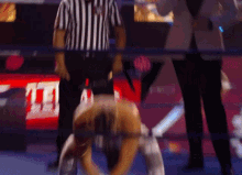 a referee stands behind a wrestler in a ring with the word tna on the screen behind him