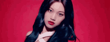 a woman with long black hair and red lipstick is standing in front of a red background and looking at the camera .