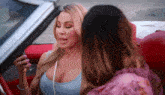 two women are sitting in a red convertible car talking to each other