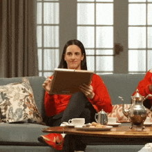 a woman in a red sweater is sitting on a couch reading a book