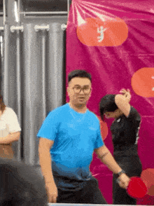 a man in a blue shirt is holding a ping pong paddle while standing on a table .