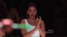a woman in a white tank top is clapping her hands in the dark .