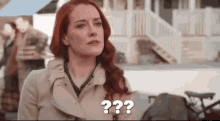 a woman with red hair is wearing a trench coat and making a funny face .