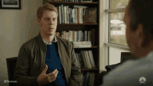 a man in a green jacket is talking to another man in a blue sweater .