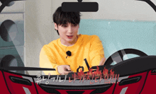 a man in a yellow shirt is driving a red car with korean writing on it