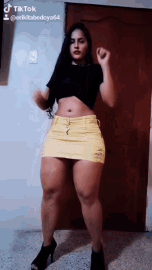 a woman in a short yellow skirt and black top is dancing .